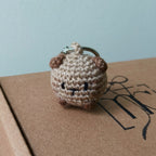 Small crocheted brown and beige keychain on a cardboard surface with a light blue background