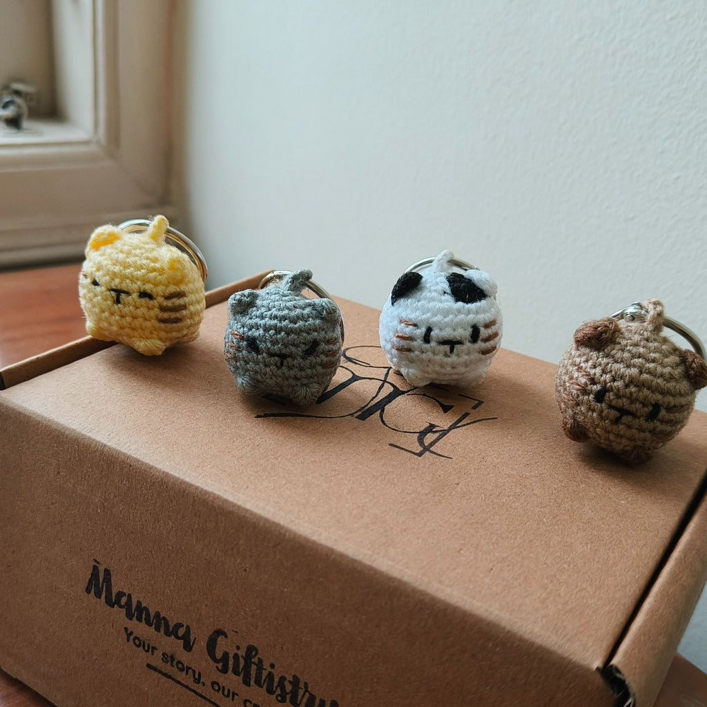 Four small crochet cat toys on a cardboard box with 'Manna Giftistry' branding.