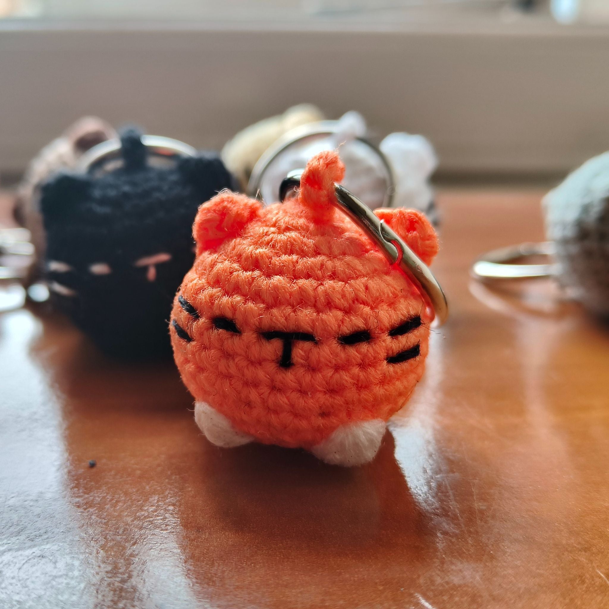 Small orange cat-shaped keychain on a wooden surface with other keychains in the background.