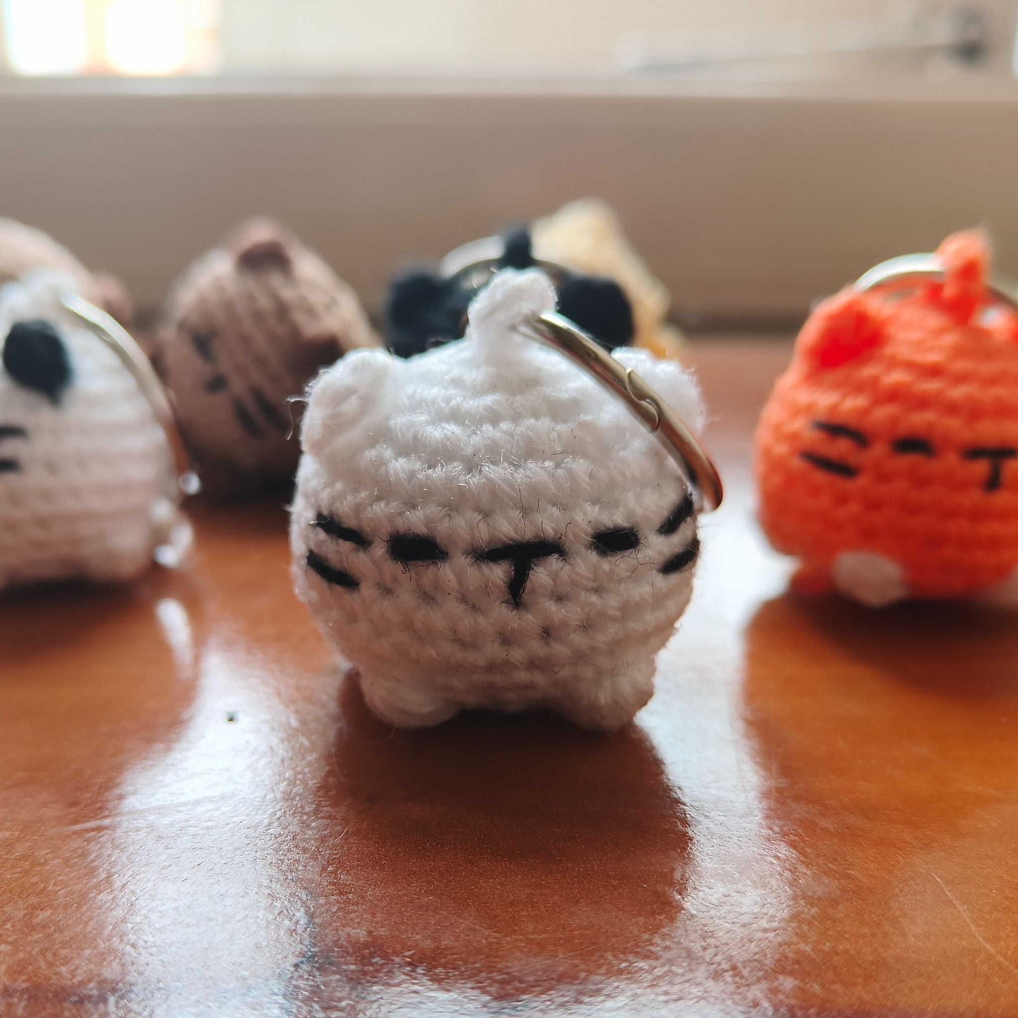 Small crocheted white cat keychain on a wooden surface