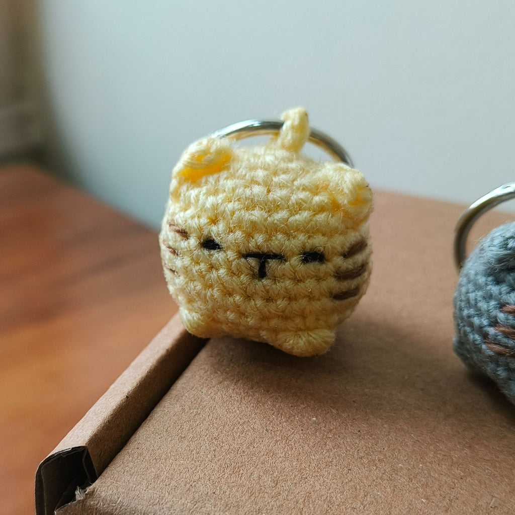 Crocheted cat keychain on a wooden surface with a blurred background
