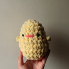 Hand holding a handmade crochet yellow plush toy against a plain background