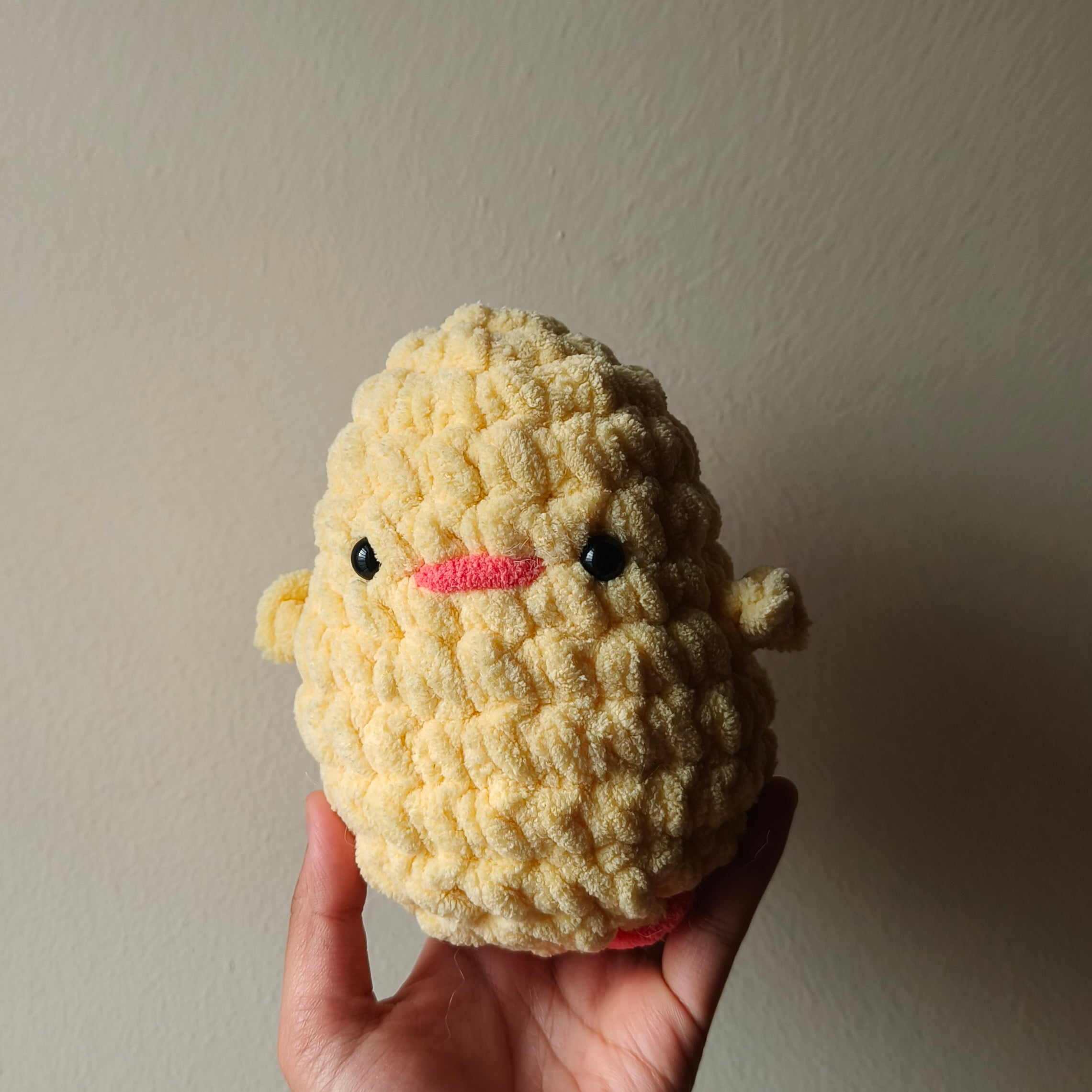 Hand holding a handmade crochet yellow plush toy against a plain background